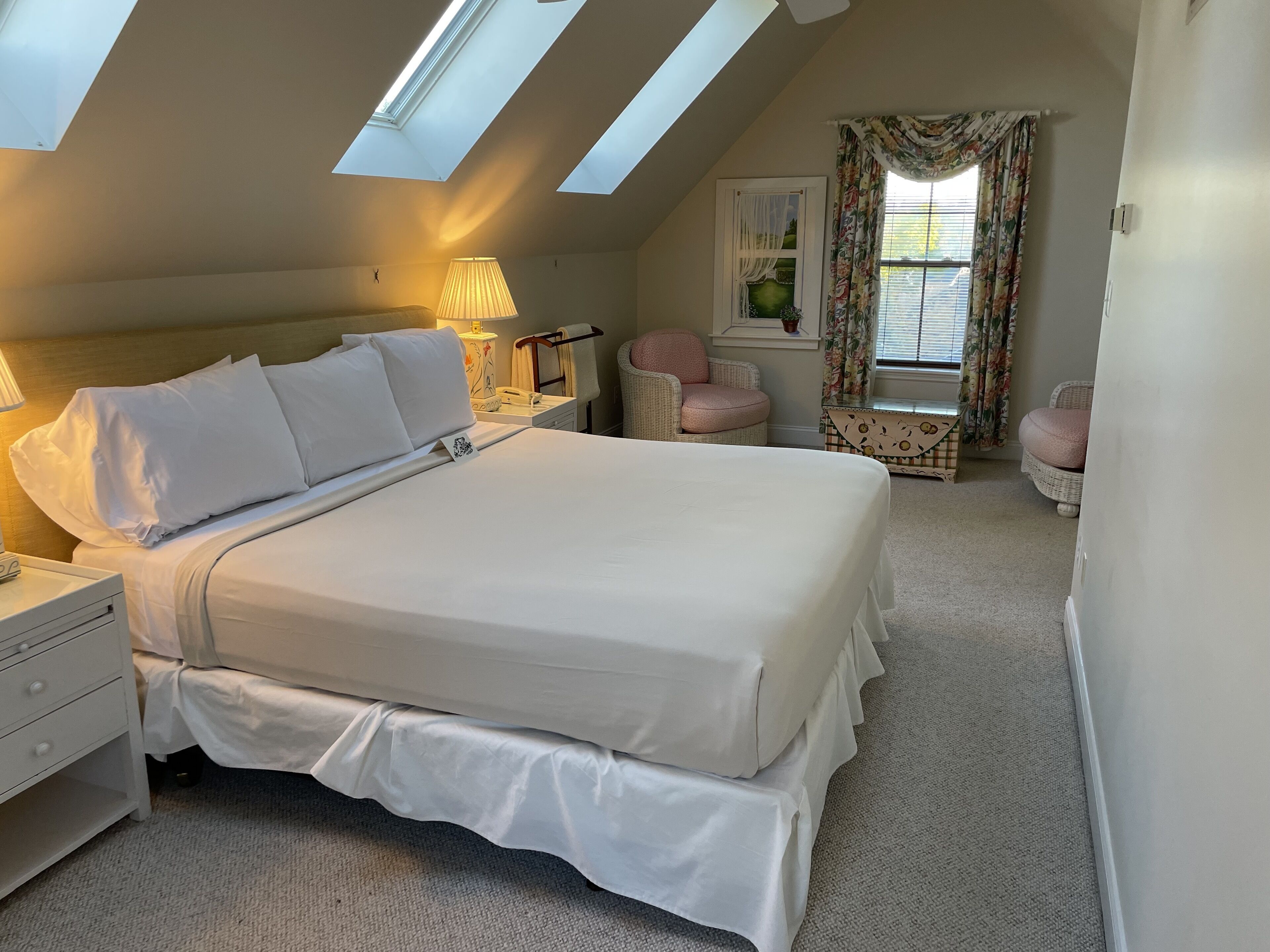 A bedroom with a large bed, a nightstand, a lamp, a chair, and a window with curtains.