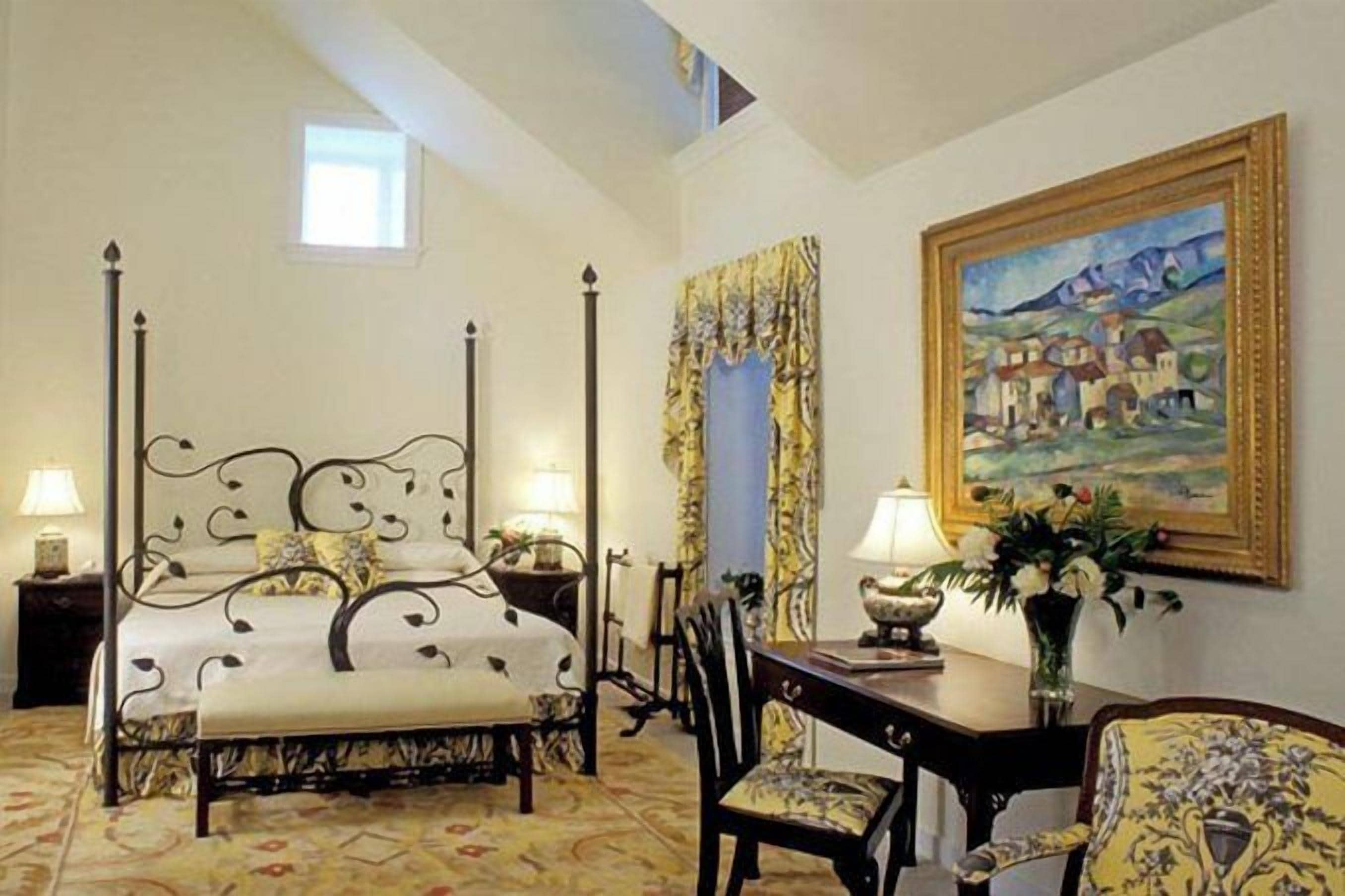 Un dormitorio con cama con dosel, una mesa de comedor con sillas, un jarrón con flores y un cuadro en la pared.