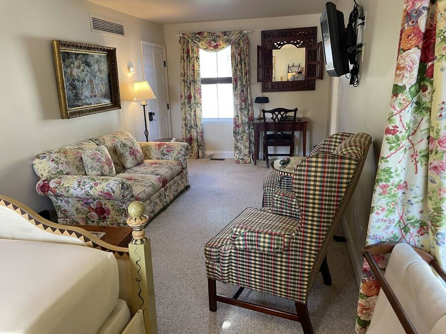 Una sala de estar con un sofá floral, un sillón a cuadros, una mesa de centro de madera y un espejo en la pared.