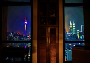 Enjoy the city view from this room, featuring two large windows with a unique split design, a wooden door, and a small shelf above.