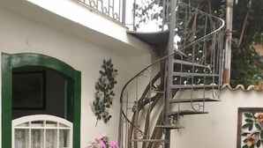 A spiral staircase leading to a balcony with a white and green exterior, surrounded by potted plants and a small garden area. - Pousada Sonho Meu (Paraty)