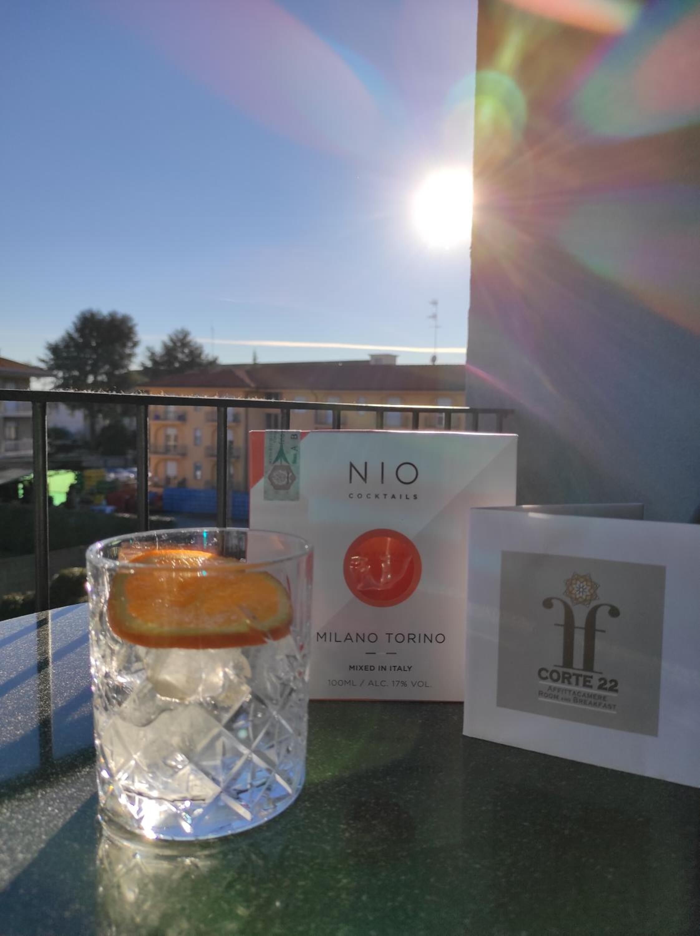 Un bicchiere con una bevanda, una confezione di cocktail NIO e un biglietto di Corte 22 su un tavolo.