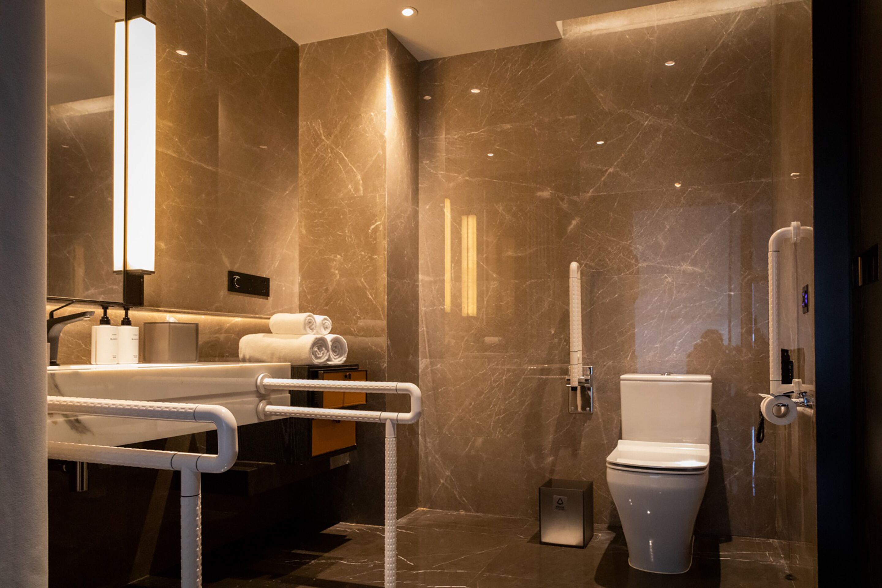 A modern bathroom with a marble wall, a white sink, a toilet, and a shower area.