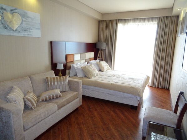 A hotel room with a bed, a sofa, a lamp, and a painting on the wall.