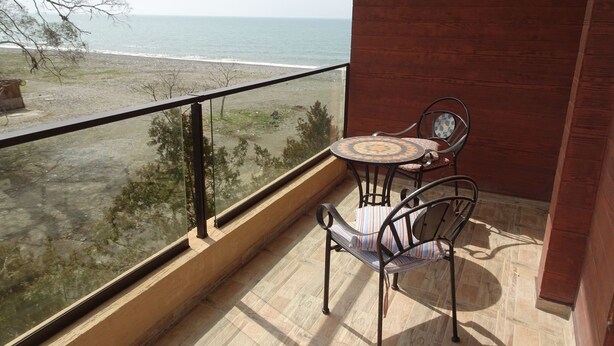 Un balcón con una mesa y dos sillas, con vista a una playa y al océano.