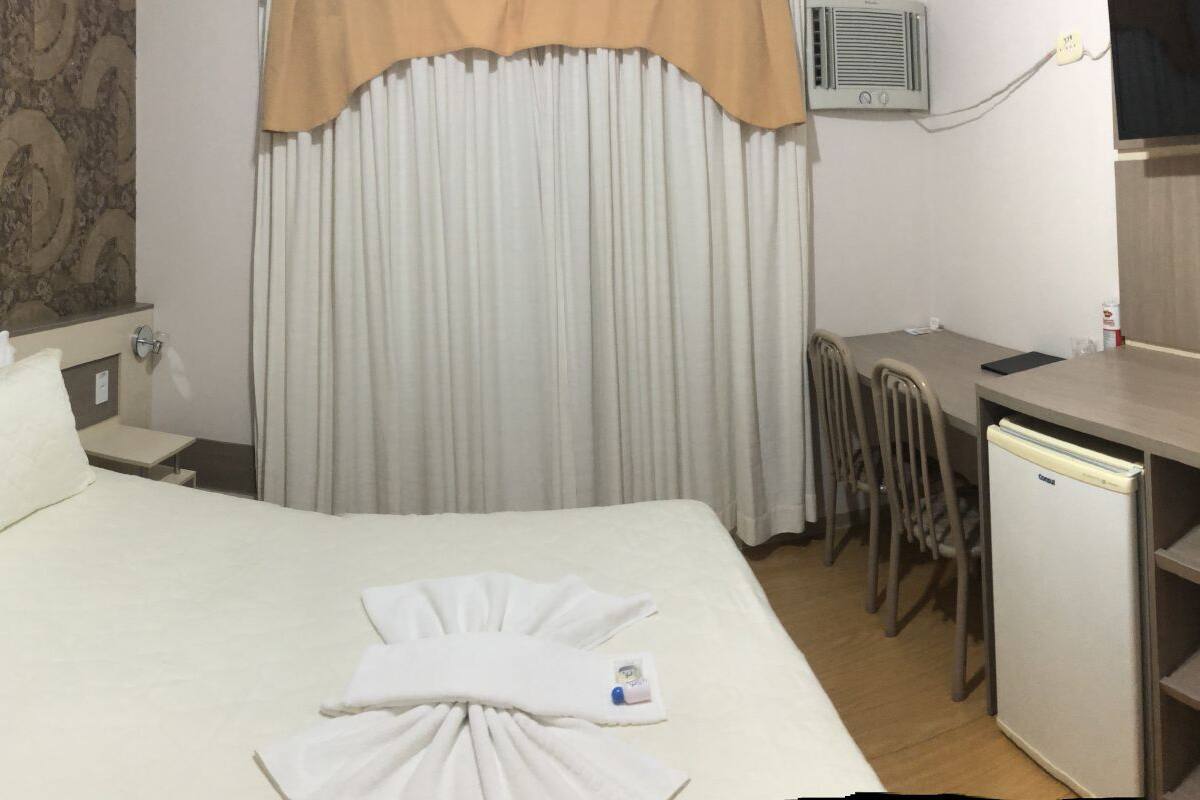 A hotel room with a bed, bedside table, desk, chairs, and a television.