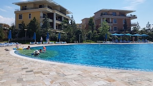A swimming pool surrounded by lounge chairs and umbrellas, with a building in the background. - Apartment on Batumskaya 16-9 ap. 22 (Batumi)