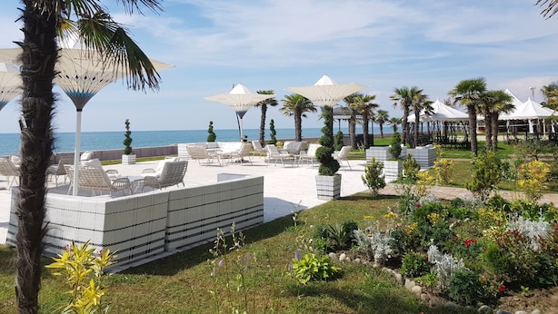 A resort with outdoor seating, palm trees, and a view of the sea. - Apartment on Batumskaya 16-9 ap. 22 (Batumi)