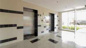 A modern lobby with a tiled floor, a glass door leading outside, and a wall-mounted elevator. - OYO Flagship 1260 Sentraland Karawang (Karawang)