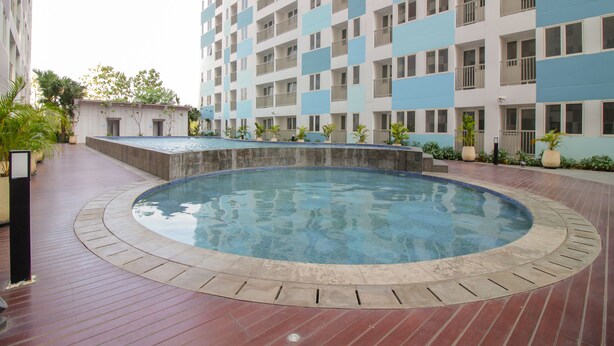 A swimming pool with a tiled deck, surrounded by a high-rise building with balconies. - OYO Flagship 1260 Sentraland Karawang (Karawang)
