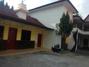 A two-story building with a red-tiled roof, a white exterior, and a small garden area with a potted plant. - Wisma Tuluy (Pematangsiantar)