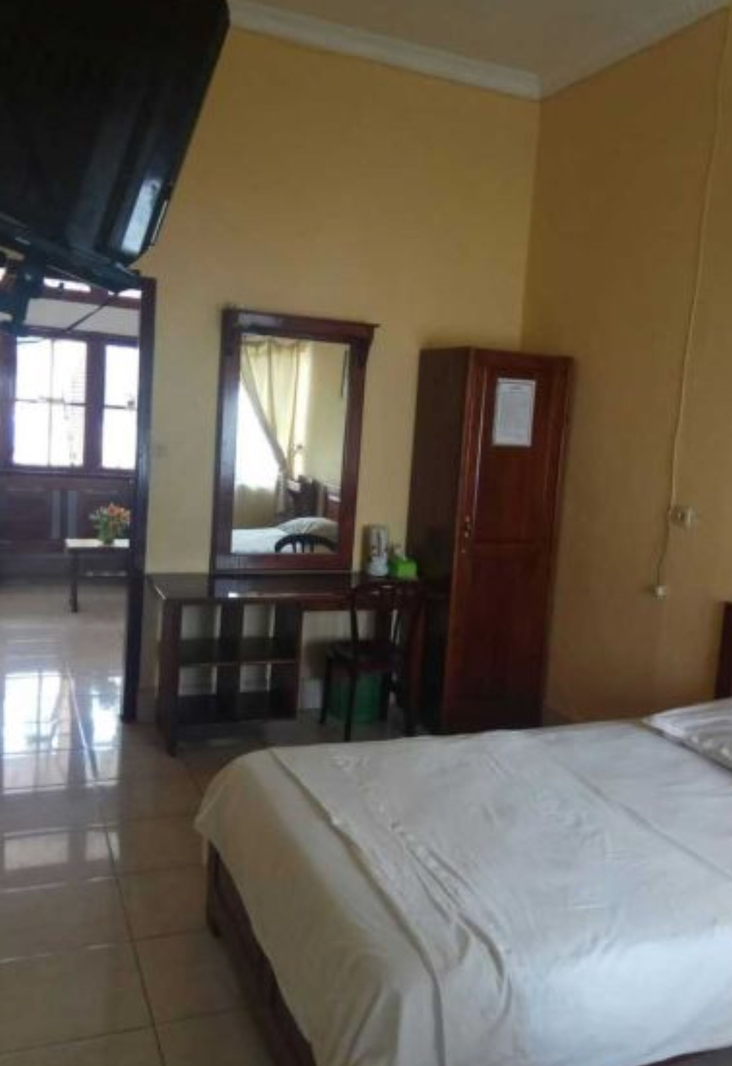 A hotel room with a bed, a desk, a chair, a wardrobe, and a mirror.