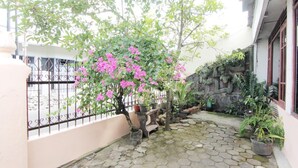 A courtyard with a pink flowering tree, a stone-tiled floor, and a stone wall. - Wisma Sarjana Syariah - Khusus Putri (Depok)