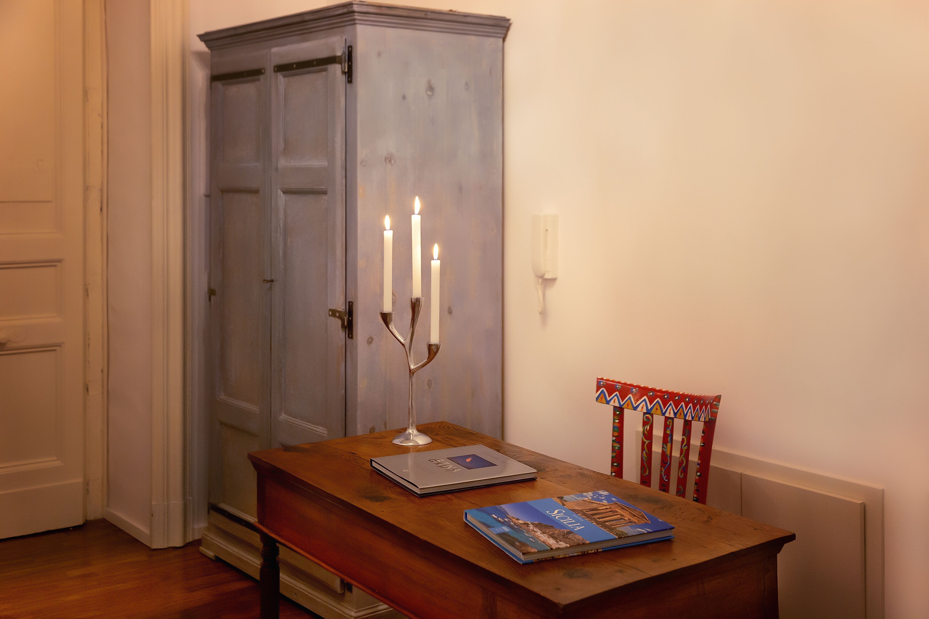 A wooden table with a laptop and a book, a cabinet, and a chair with a patterned cushion.