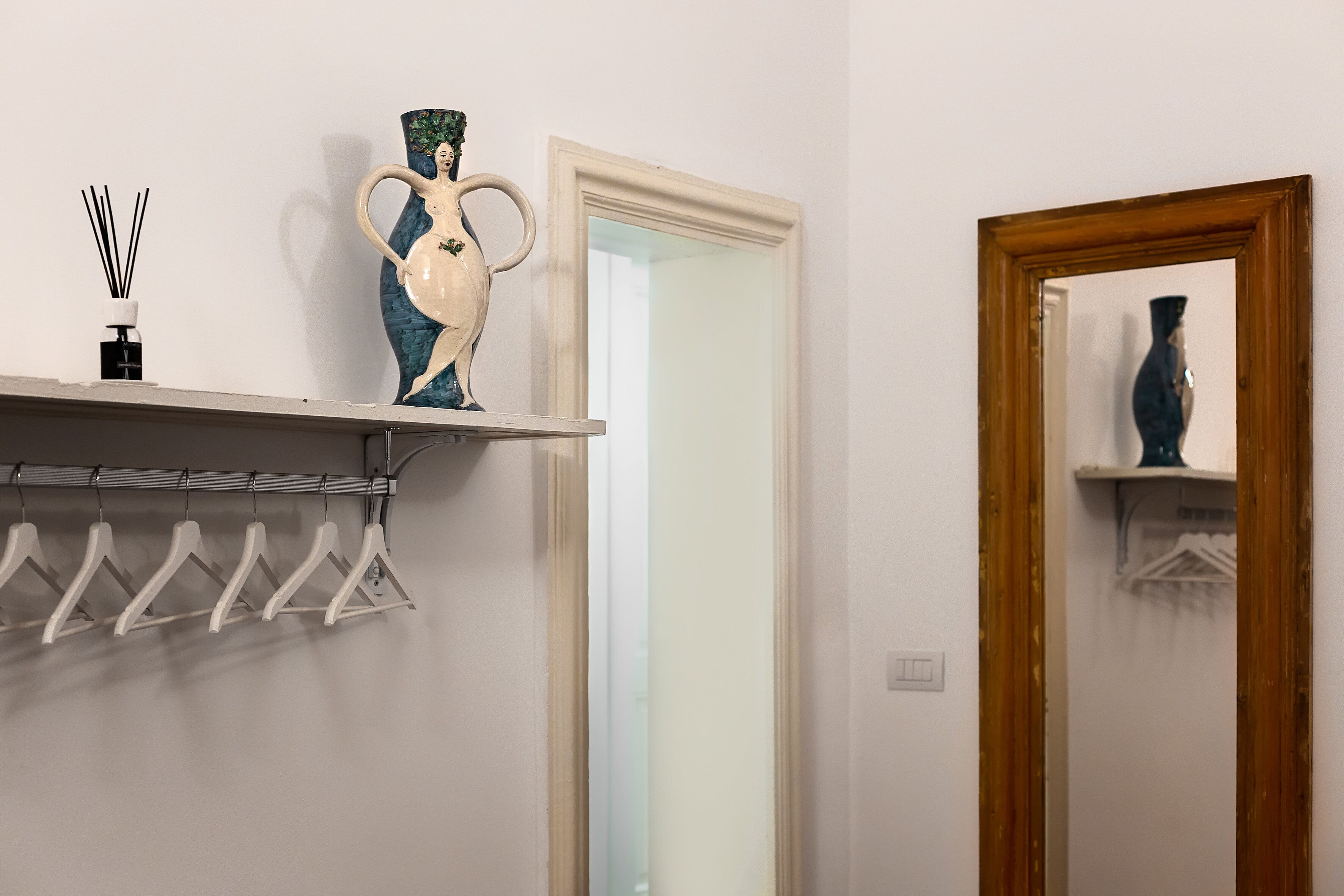 A bathroom with a mirror, a shelf with a vase, and a rack of white hangers.