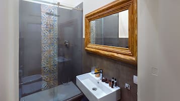Een badkamer met een douchecabine van glas, een wit wastafelmeubel met een spiegel erboven en betegelde muren.