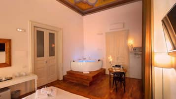 A hotel room with a large bathtub, a dining area with a table and chairs, and a bed with towels.