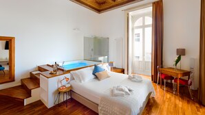 A hotel room with a large bed, a desk, a chair, a small table, a mirror, a window, and a staircase. - Naca Suite (Catania)