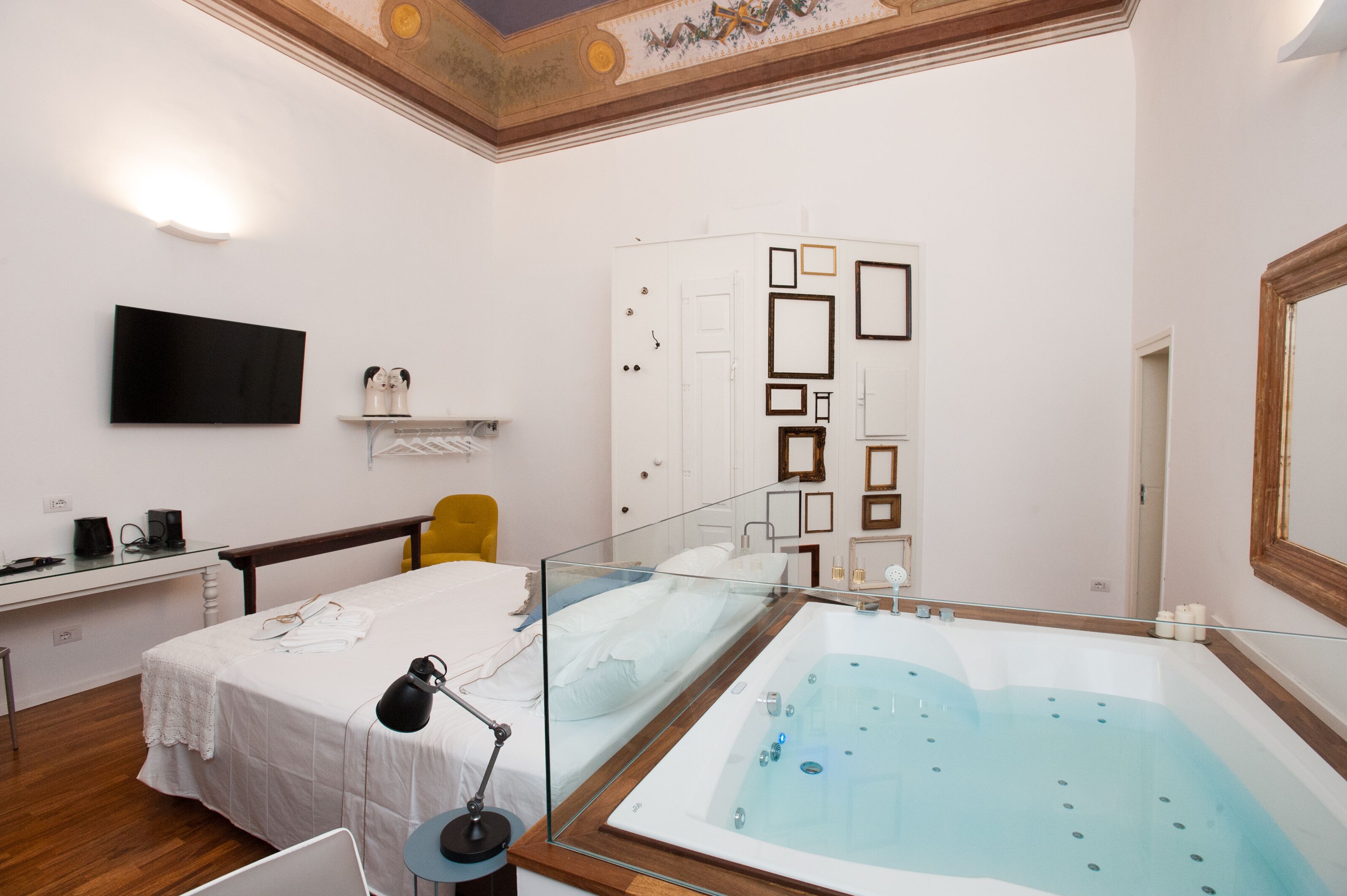 Habitación de hotel moderna con una bañera grande, un televisor de pantalla plana, un escritorio con una silla y una cama con cubrecama blanco.