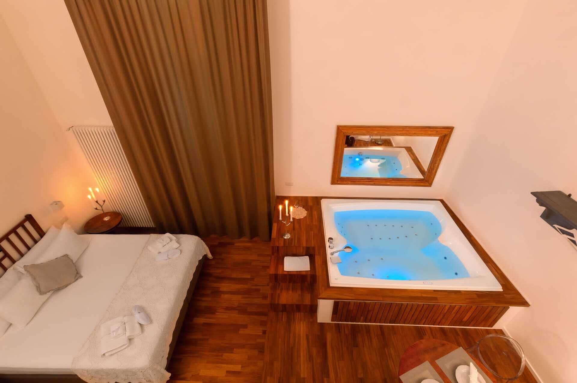 A hotel room with a bed, a wooden vanity with a bathtub, a mirror, and a nightstand with a lamp.