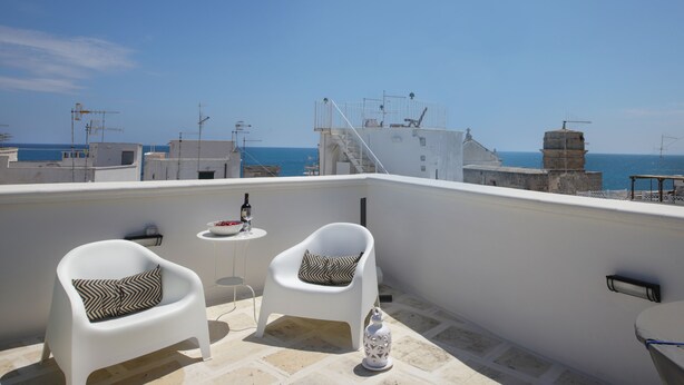 Terraza en la azotea con dos sillas blancas y una mesita pequeña, con vistas al mar.