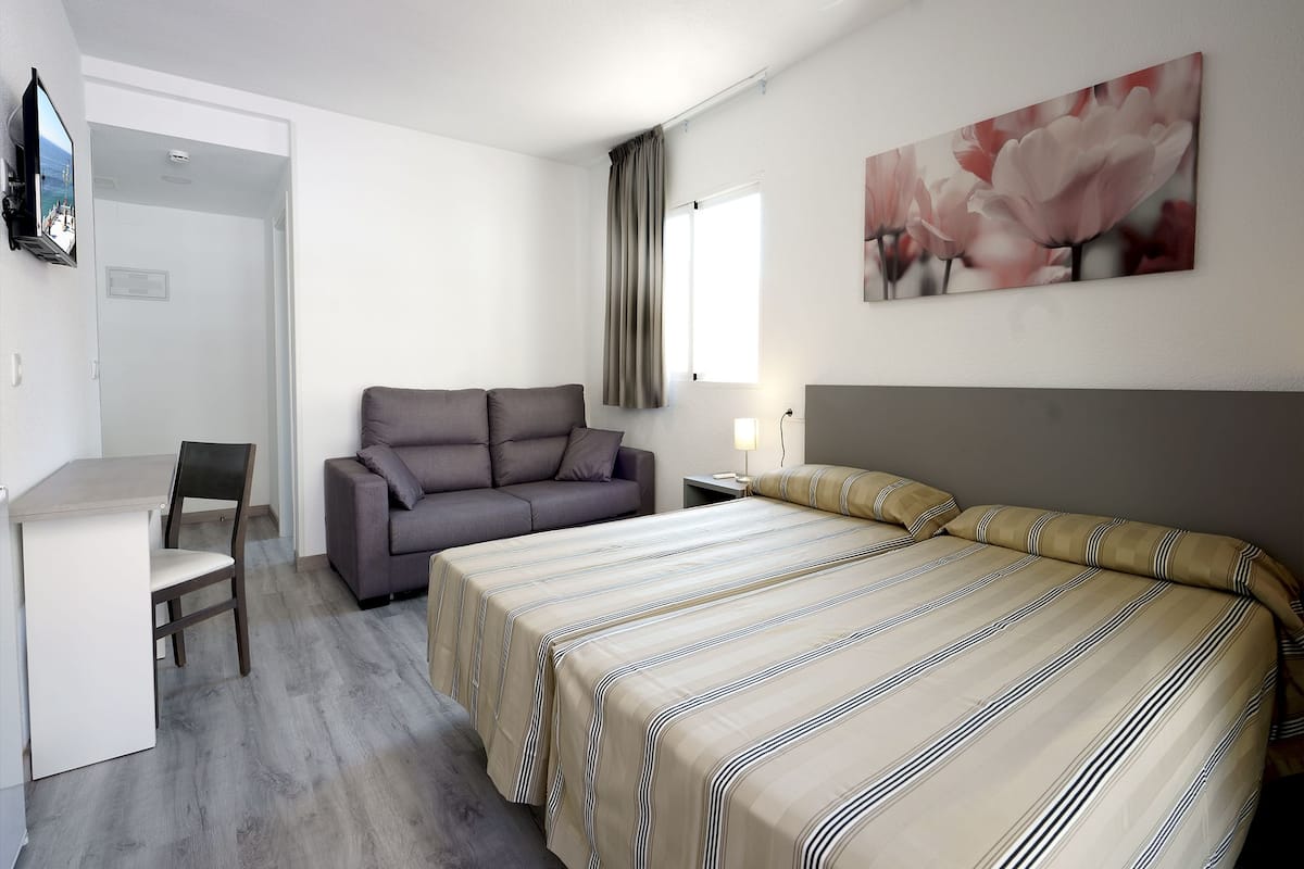 A hotel room with a bed, a sofa, a desk, and a TV.
