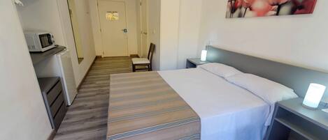 A hotel room with a bed, bedside table, chair, and a microwave on a counter.