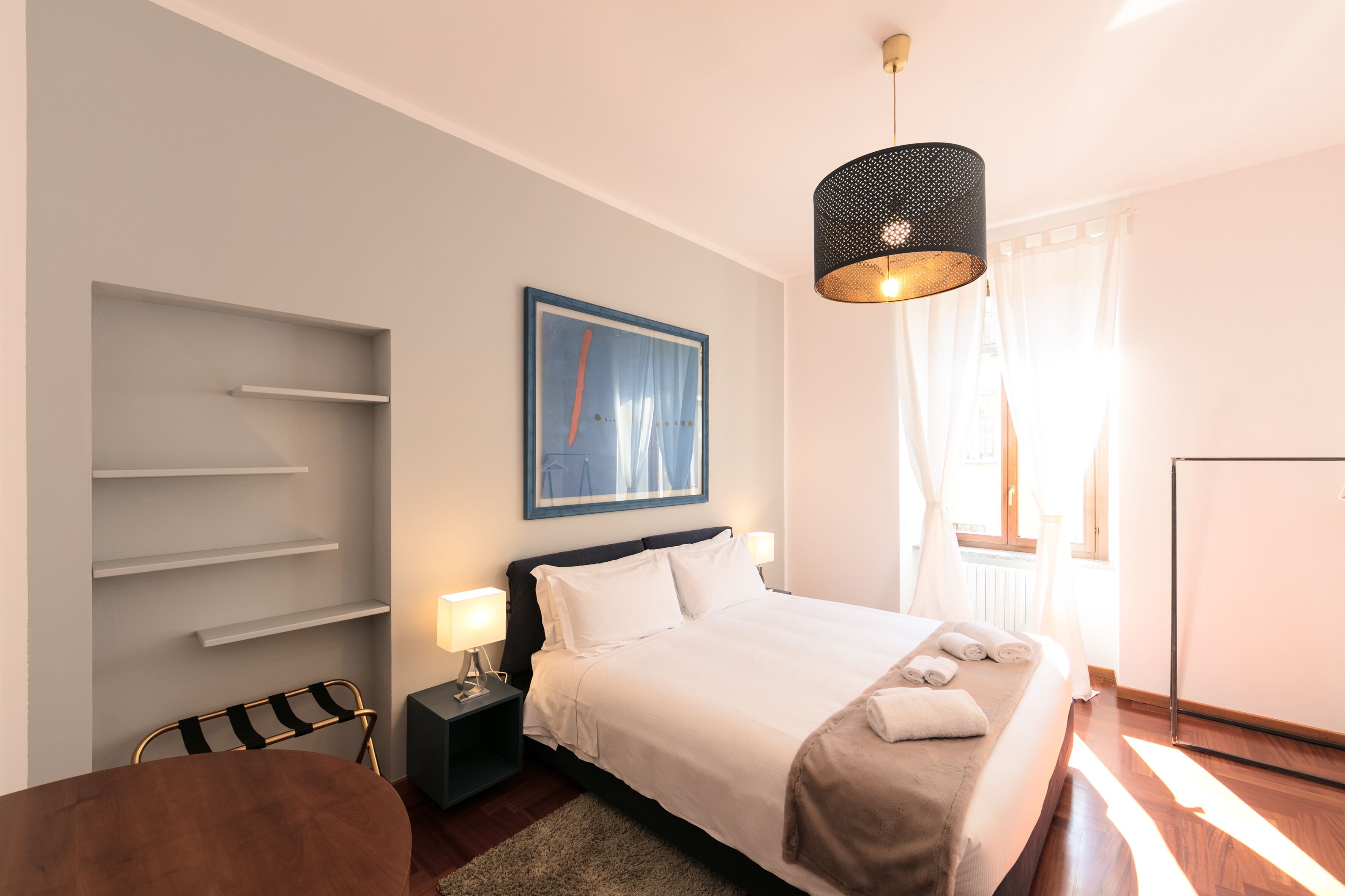 A neatly arranged hotel room with a bed, bedside tables, a chair, and a desk.