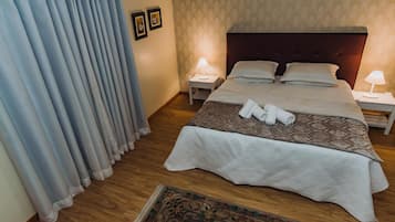 Cama bem arrumada com colcha estampada, duas luminárias de cabeceira e um par de toalhas sobre a cama.