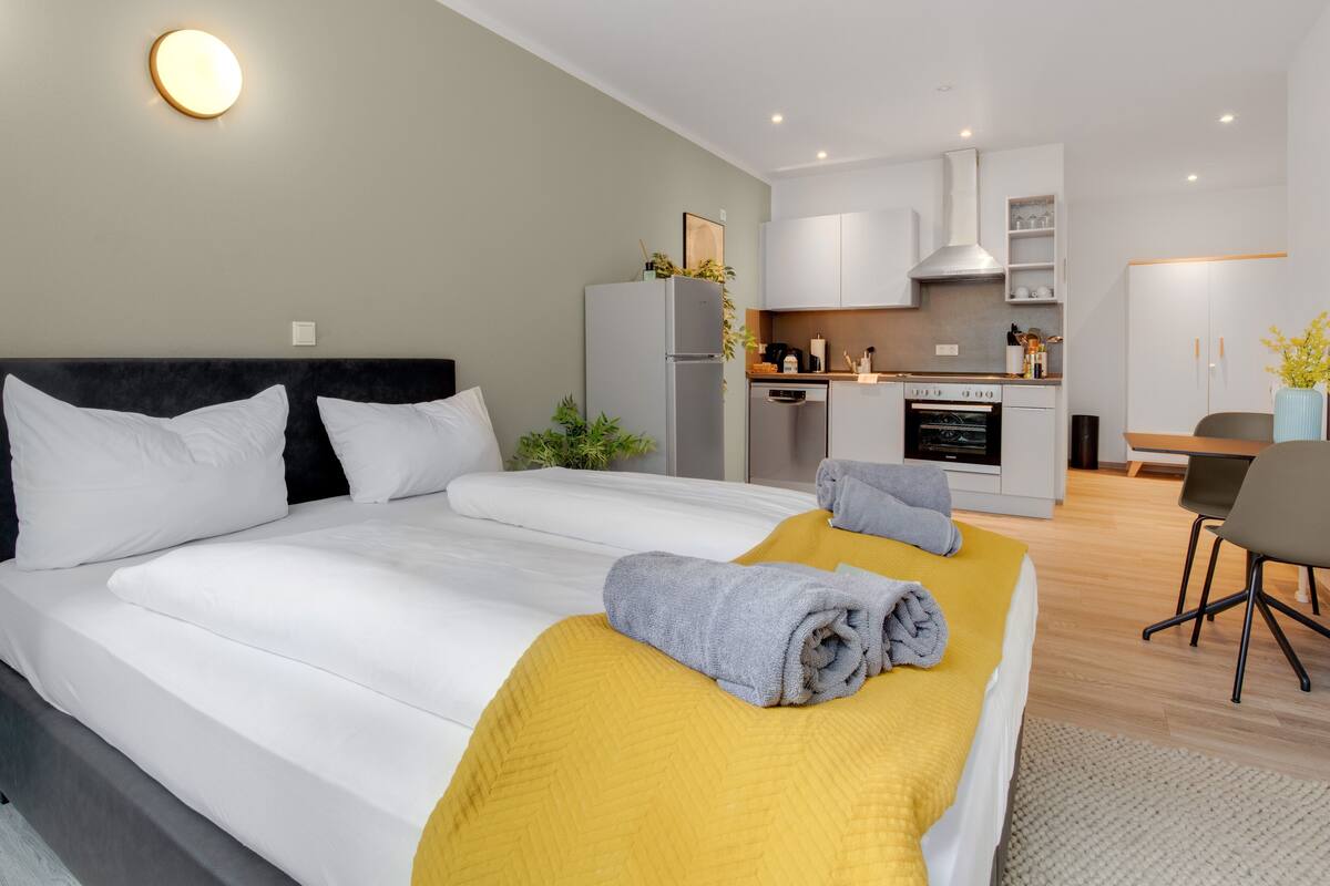 Ein modernes Hotelzimmer mit einem großen Bett, einer kleinen Küchenzeile und einem Esstisch.