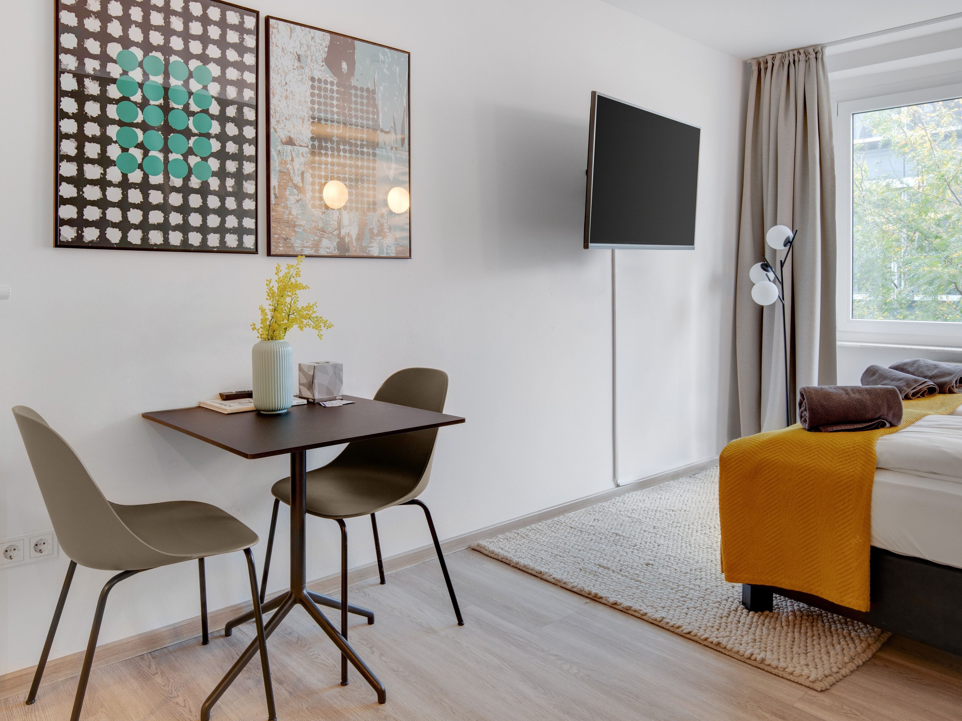 Ein Hotelzimmer mit einem Bett, einem Schreibtisch mit Stühlen, einem Flachbildfernseher und Bildern an der Wand.