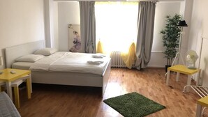 Ein Schlafzimmer mit Bett, Nachttisch, Stuhl, Heizkörper, einem Fenster mit Vorhängen und einer Pflanze.