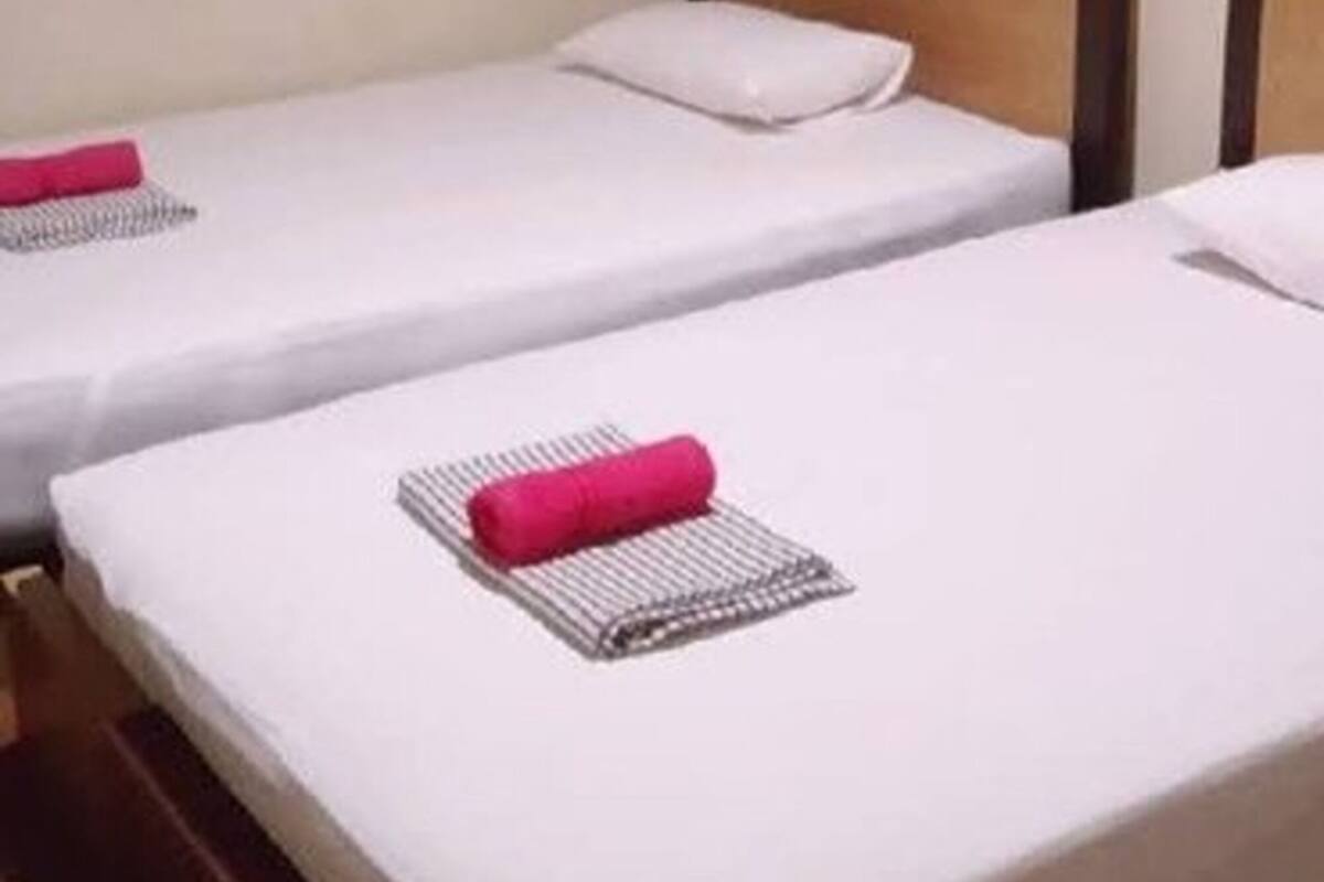 A hotel room with two single beds, a wall-mounted air conditioner, a framed picture, and a brown curtain.