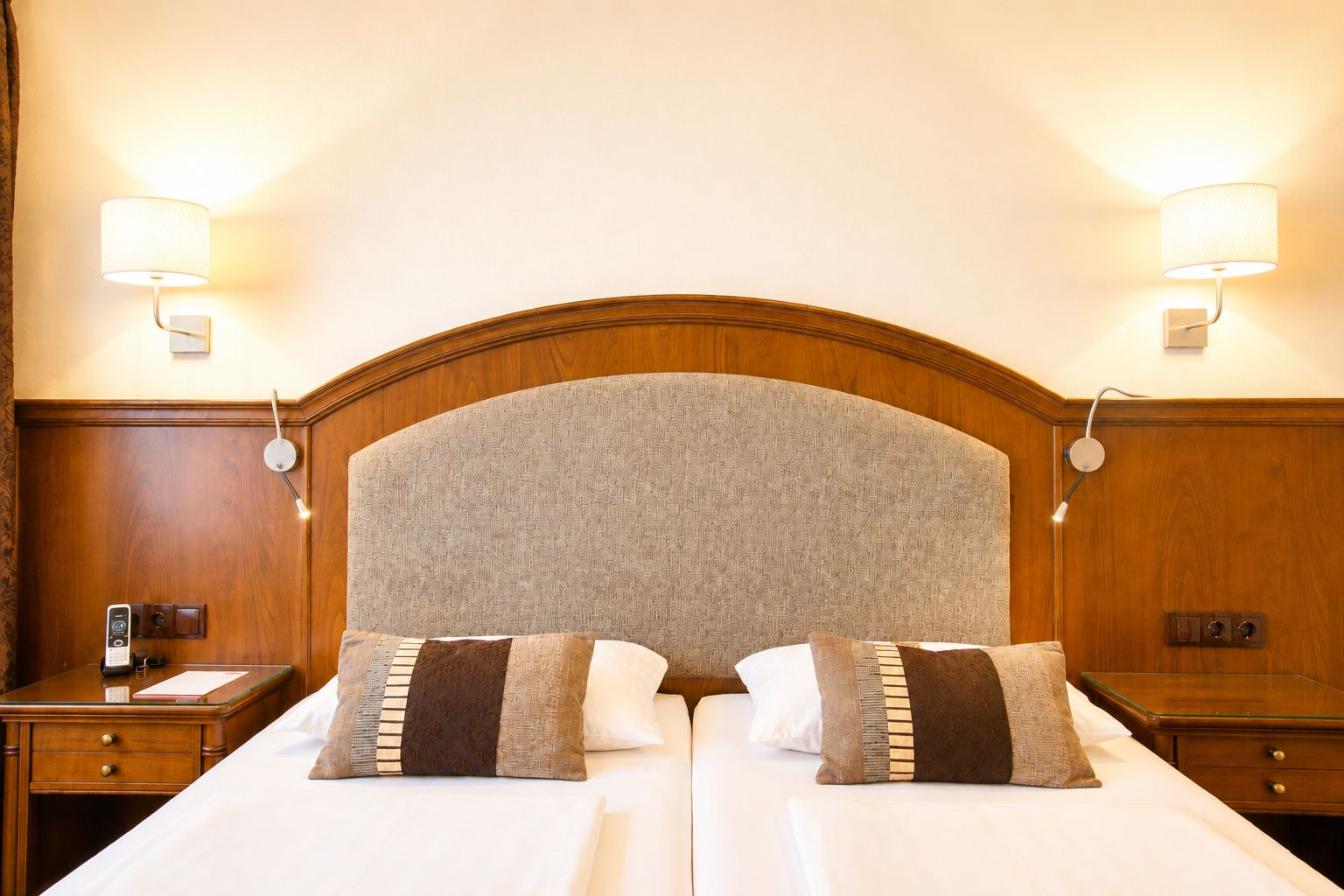 A hotel room with a large bed, two bedside tables, and wall-mounted lamps.