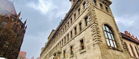 Un edificio histórico de piedra con un gran ventanal de arco y una torre en esquina.