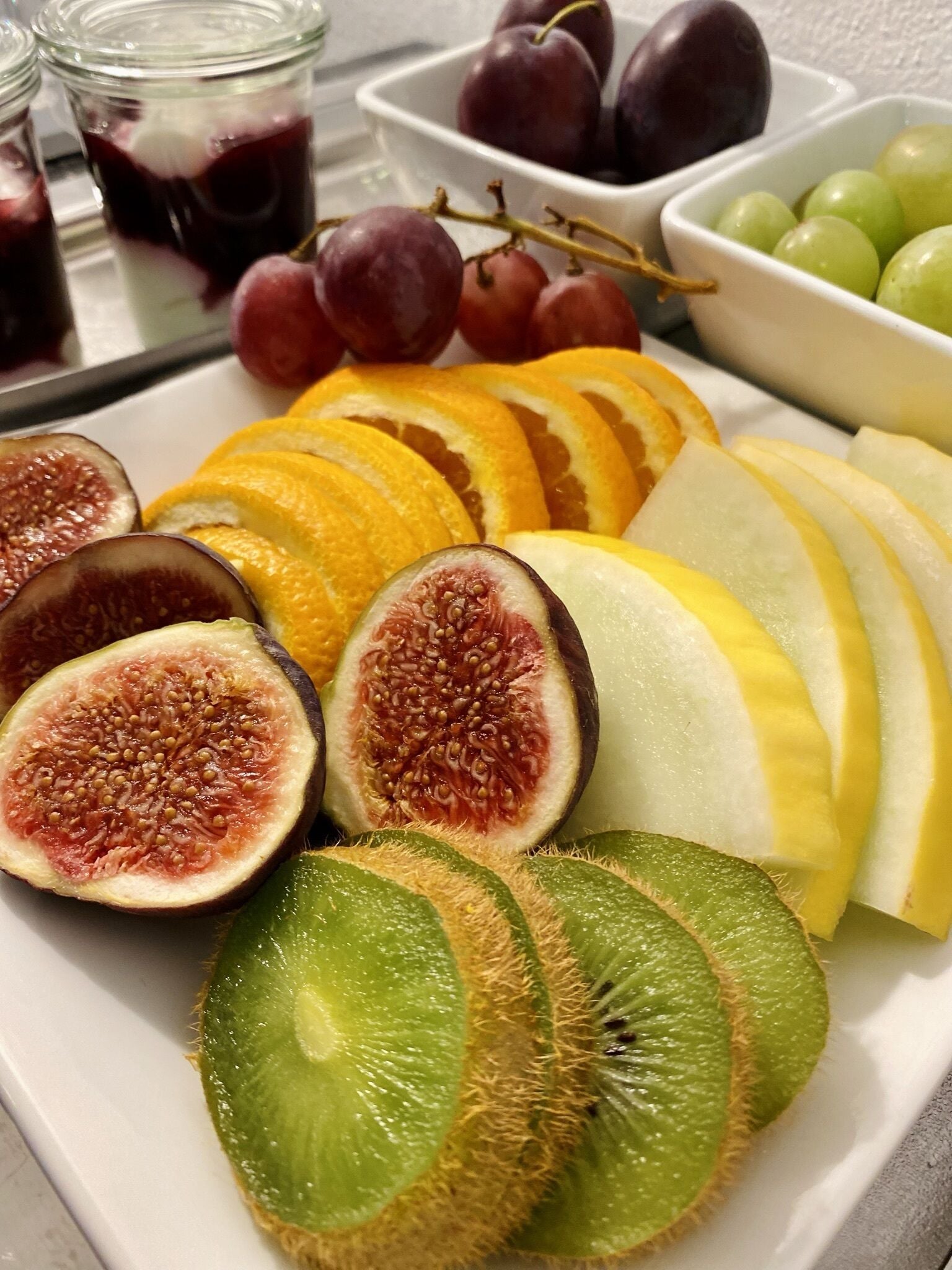 A safata de fruita amb taronja tallada, kiwi, figues, raïm i présims.