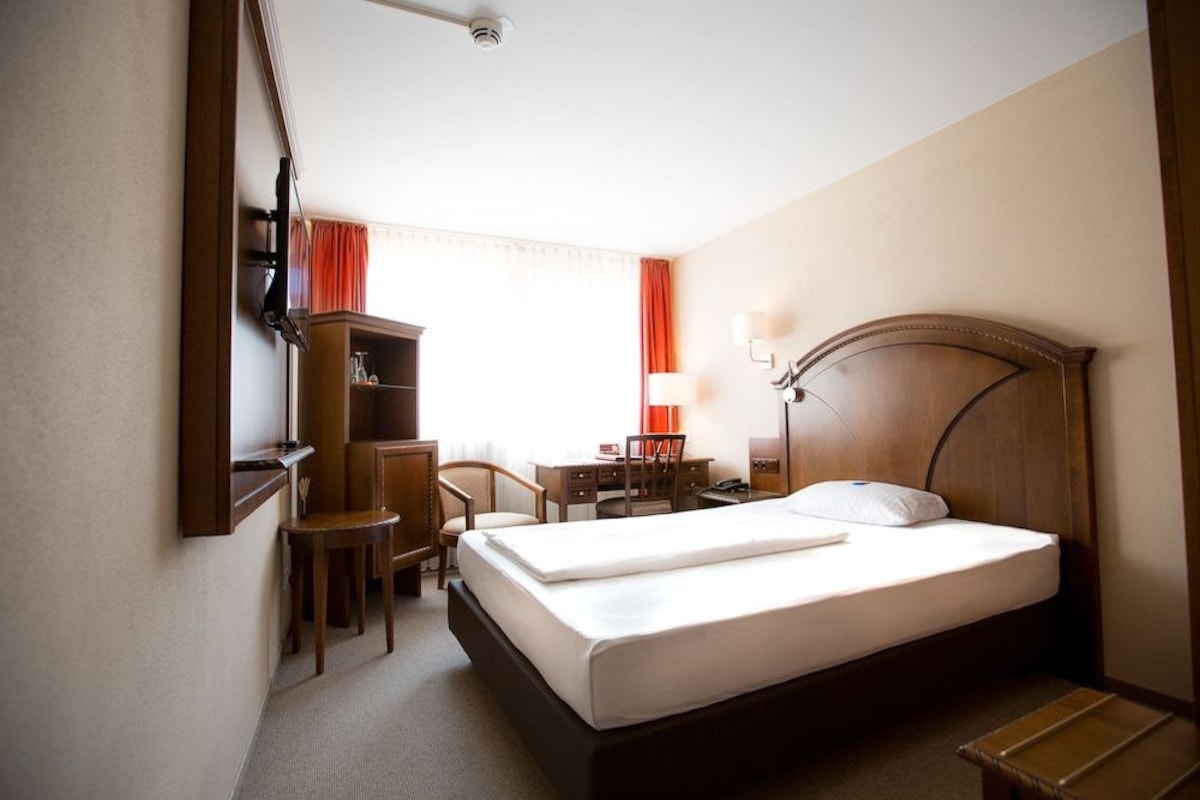 A hotel room with a bed, desk, chair, and a small cabinet.