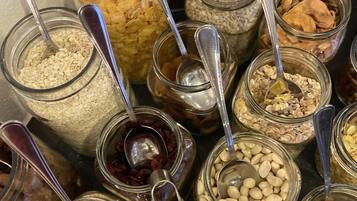 A variety of food items in glass jars with spoons, including oats, nuts, and dried fruits.