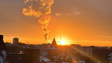 Un paisaje urbano al atardecer, con edificios silueteados contra el cielo, destacando una chimenea que emite humo.