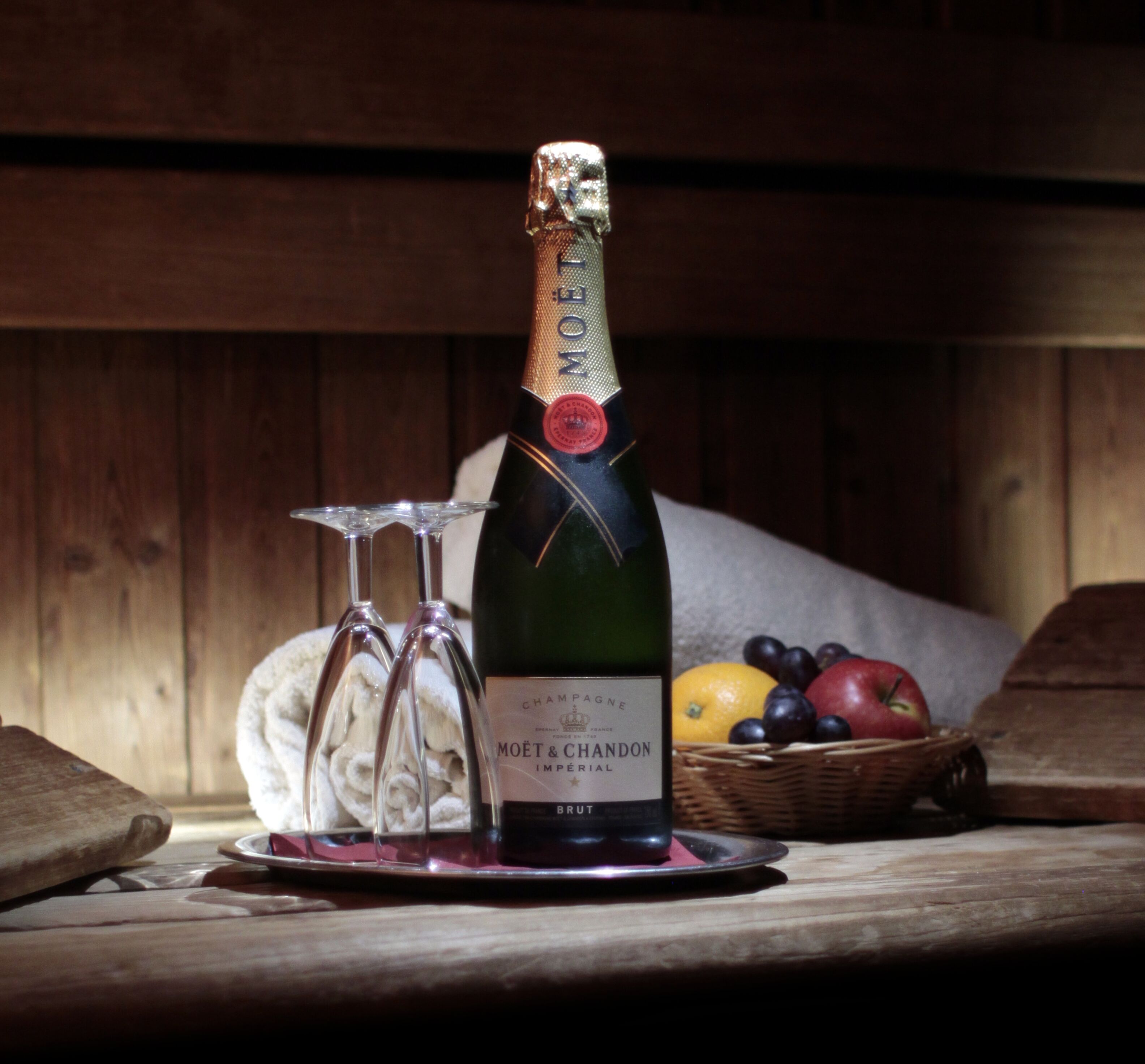Una botella de Moët & Chandon, una copa y una cesta de frutas sobre una mesa de madera.
