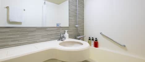Un baño moderno con lavamanos curvo, un espejo grande, un cabezal de ducha de mano y una barra de apoyo.