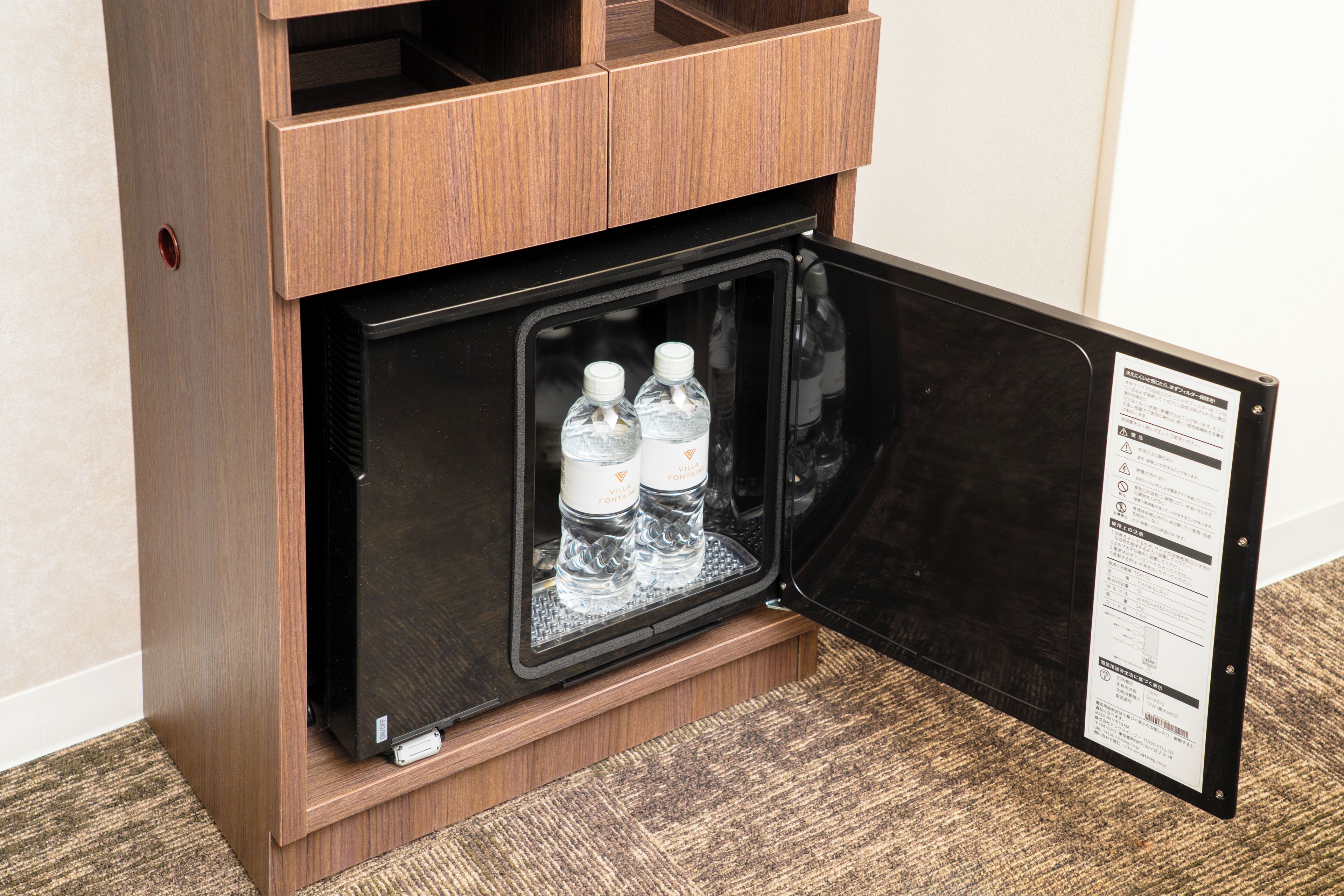 A minibar with a wooden exterior and a black interior, containing two bottles of water.