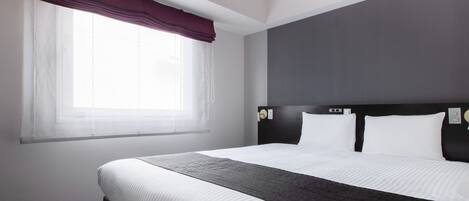 Habitación de hotel con una cama grande, una ventana con cortinas translúcidas, un cabecero oscuro y una paleta de colores neutros.