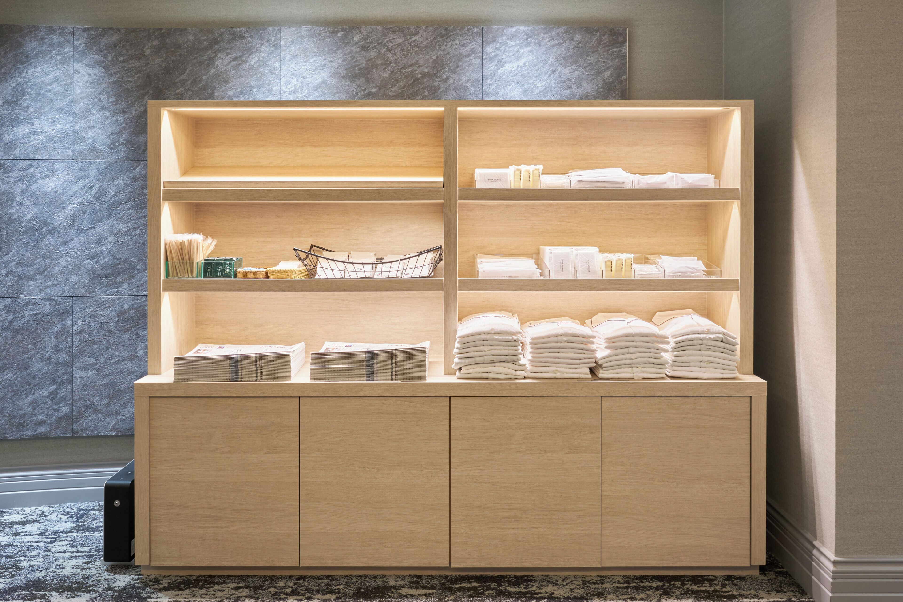 A wooden cabinet with multiple shelves, some holding folded towels and others with books and a basket.