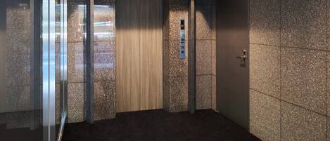 A modern elevator with a control panel, glass walls, and a carpeted floor.