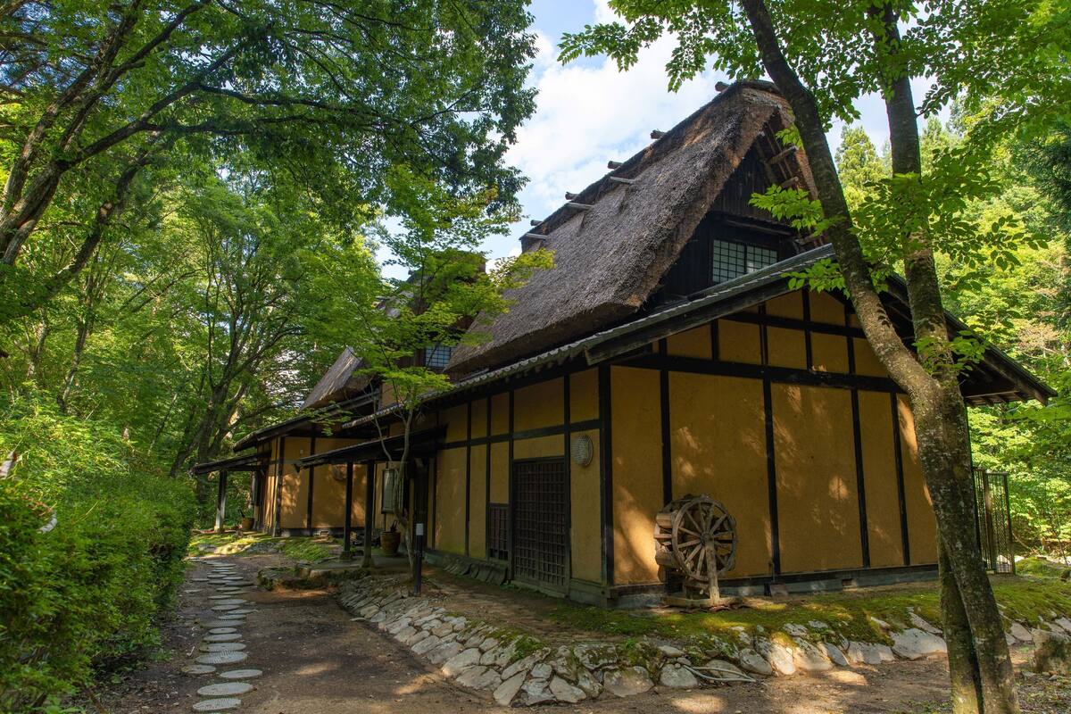 A traditional Japanese building with a thatched roof, surrounded by lush greenery.