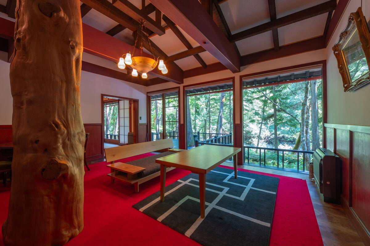 A spacious room with a large wooden tree trunk, a wooden table, benches, and a red carpet.