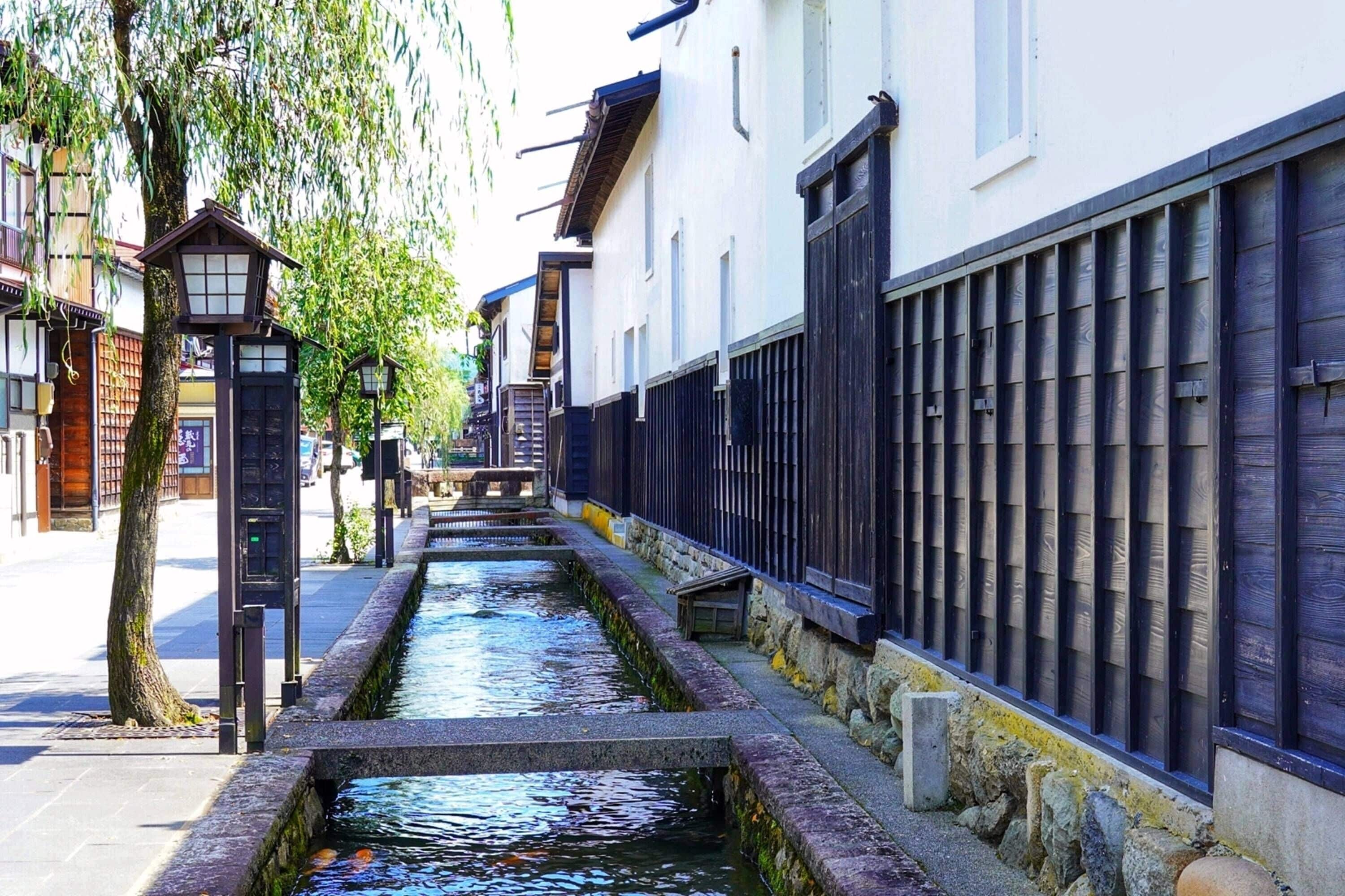 A narrow water channel flanked by traditional buildings with wooden shutters and a stone wall.