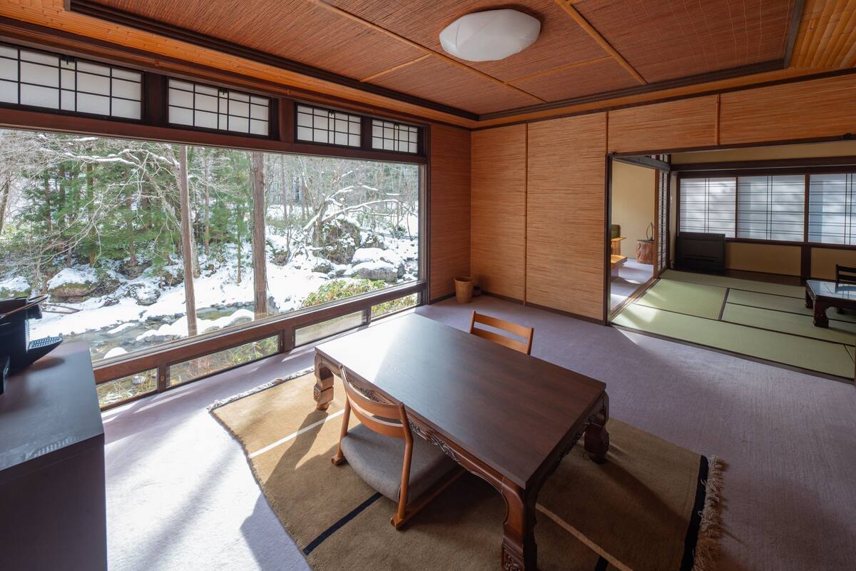 A traditional Japanese room with tatami flooring, a wooden table, and a view of a snowy landscape.