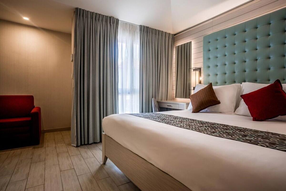 Habitació d'hotel amb un llit gran, un butacó vermell, una tauleta de nit i un panell de llit amb borrons.